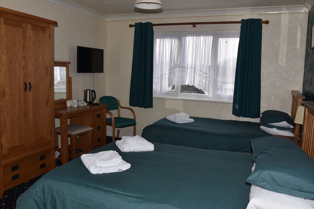 A hotel room with two beds, a wooden wardrobe, a desk with a chair, and a television on the wall.
