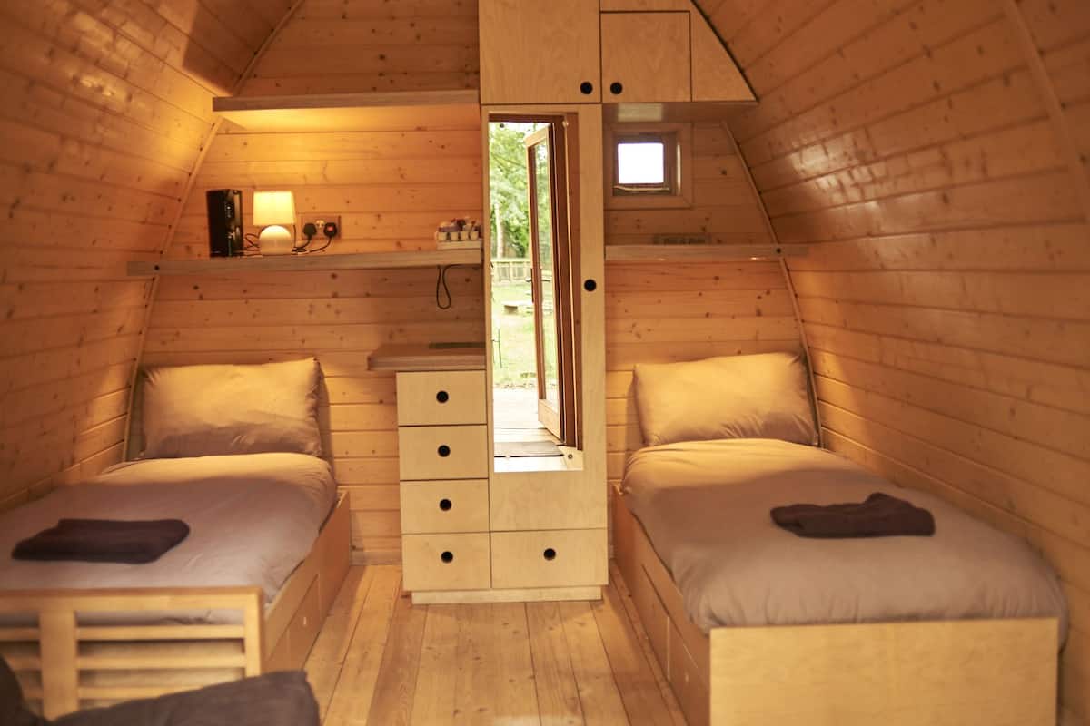 A cozy attic bedroom with two beds, a small dresser, and a window providing a view of the outdoors.