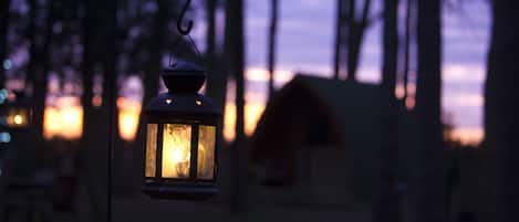 A lantern hanging in a forested area with a blurred background of trees and a distant building.