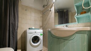 Egy kis méretű fürdőszoba mosógéppel, mosdókagylóval és WC-vel felszerelve.