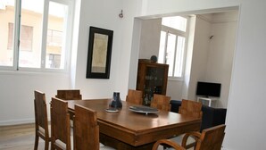 A dining area with a wooden table and chairs, a cabinet with glass doors, and a television on a stand. - Neoclassical ART-House Bhive (Athens)