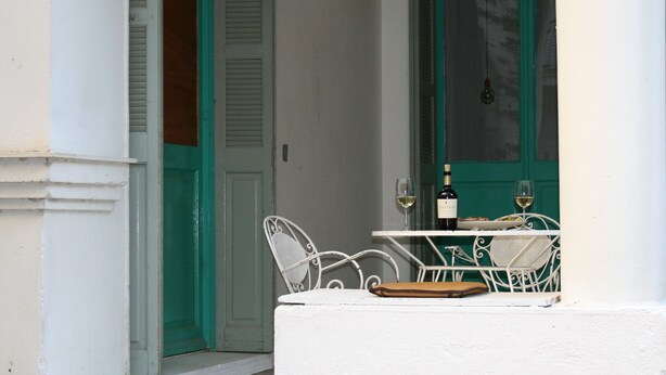 A white balcony with a table and chairs, a bottle of wine, and a glass of wine. - Neoclassical ART-House Bhive (Athens)