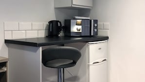 A compact kitchenette with a black countertop, a coffee maker, a microwave, and a small refrigerator. - No57 (Crewe)