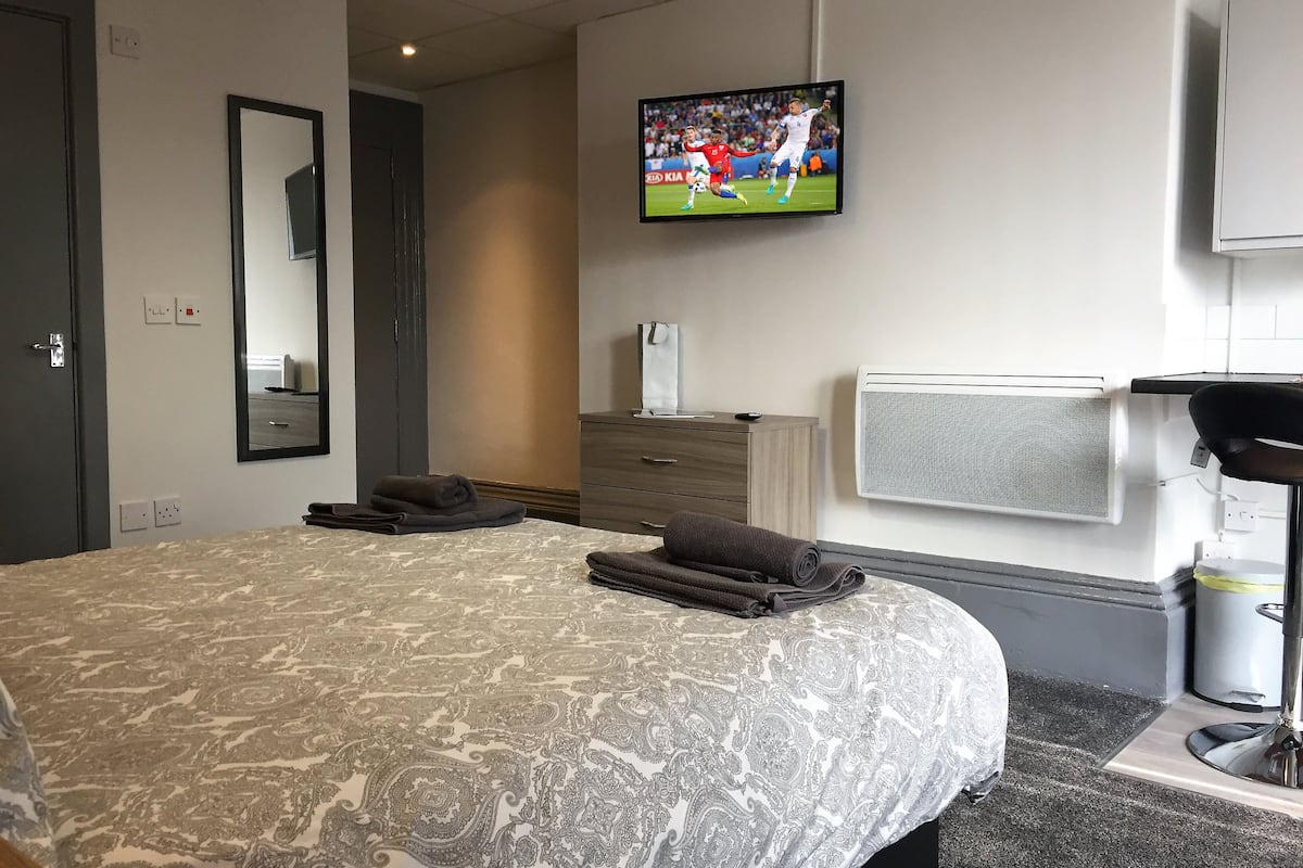 A hotel room with a large bed, a TV mounted on the wall, a dresser, and a radiator.