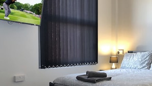 A hotel room with a bed, two bedside lamps, a nightstand, a window with blinds, and a view of a golf course. - No57 (Crewe)