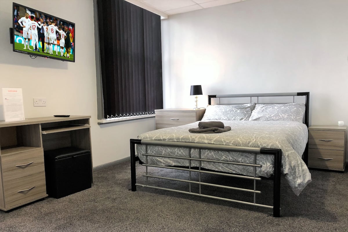 A bedroom with a bed, bedside tables, a desk, and a television displaying a sports event.