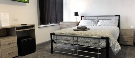 A bedroom with a bed, bedside tables, a desk, and a television displaying a sports event.