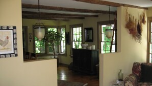 Un salon chaleureux avec un plancher en bois, un canapé à motifs floraux, une petite table sur laquelle est posé un vase, et une grande fenêtre donnant sur un paysage verdoyant.