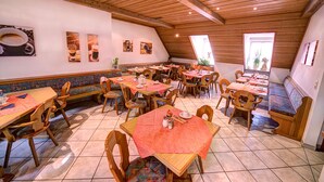 Un restaurante acogedor con mesas y bancos de madera, techo inclinado y obras de arte en las paredes.