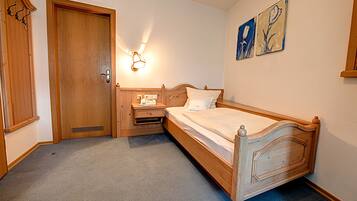 Un dormitorio con una cama de madera, una mesita de noche, una lámpara de pared y una puerta con perchero.
