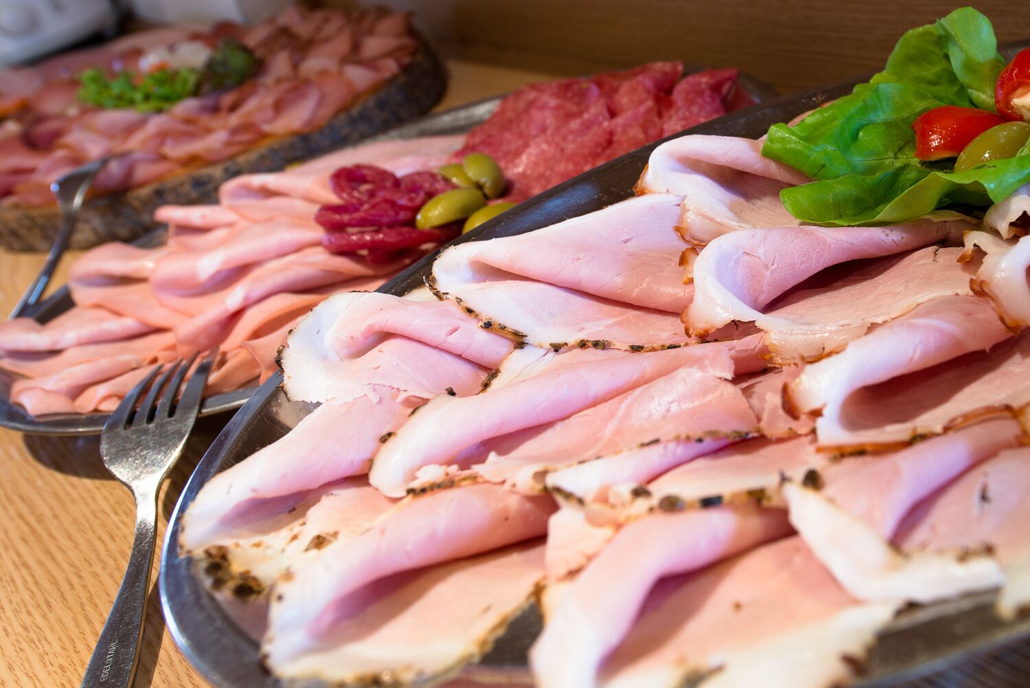 A buffet table with sliced meats, olives, and vegetables.