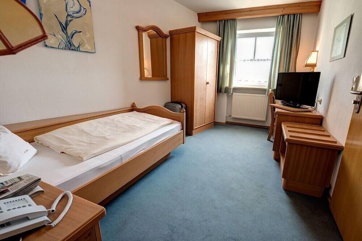 A hotel room with a single bed, a desk with a telephone, a television, and a window with curtains.
