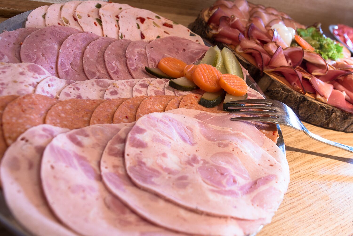 Diversos tipos de carnes fatiadas e legumes dispostos numa tábua de madeira.