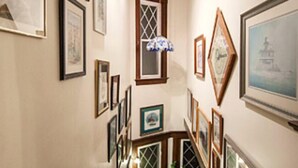 Eine Treppe mit Holzgeländern, gerahmte Kunstwerke an den Wänden und einer Chandelüstere.