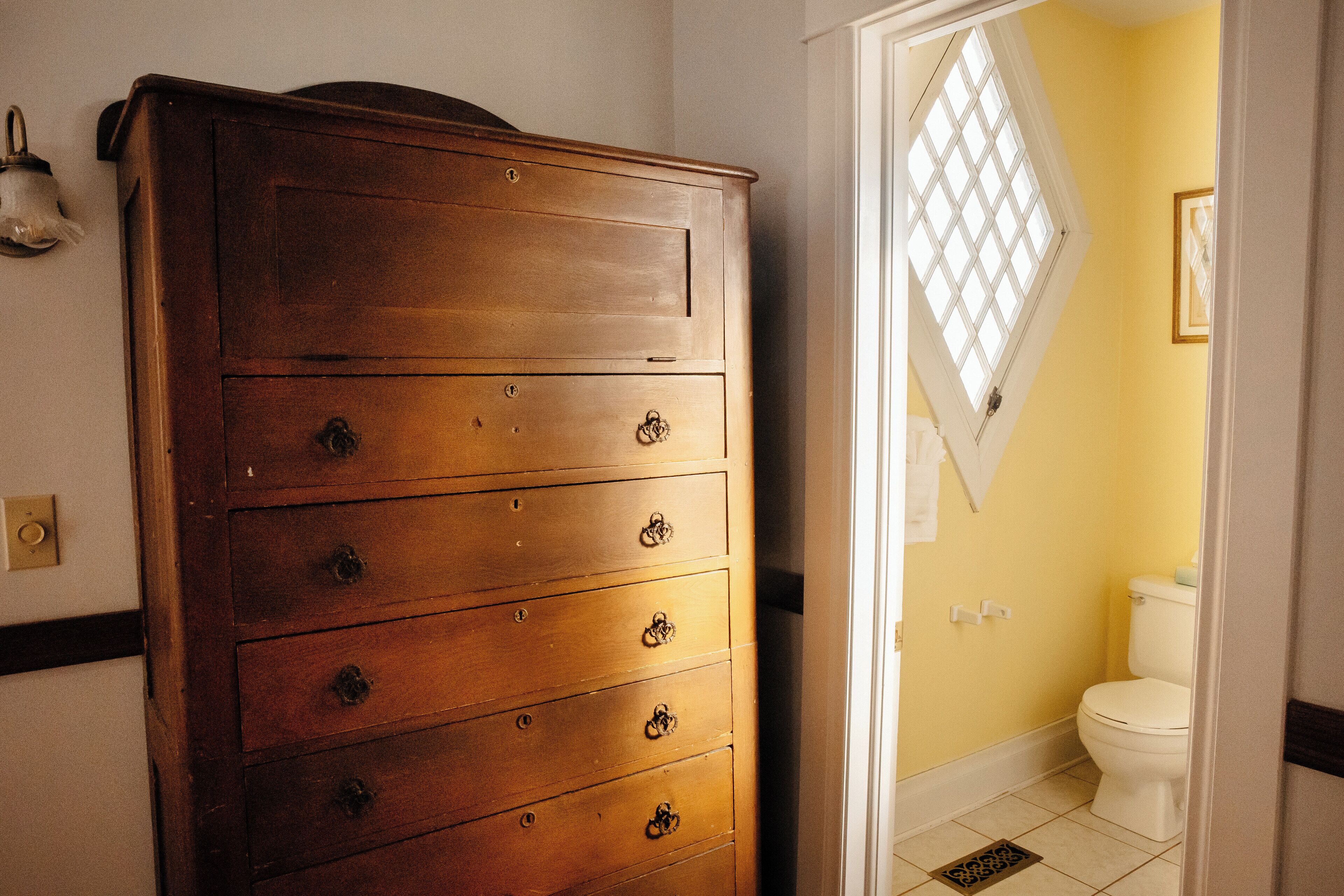 Een houten dressoir met meerdere lades in een badkamer met een gele wand en een wit toilet.