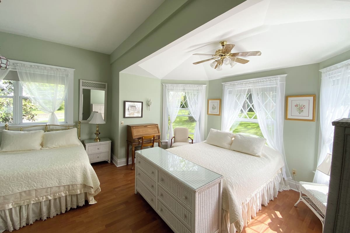 A bedroom with two beds, a ceiling fan, and a view of the garden.