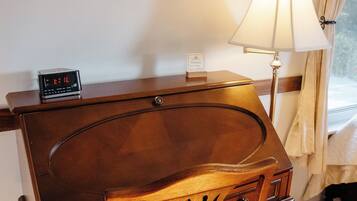A wooden desk with a lamp, a clock, and a framed picture on the wall.