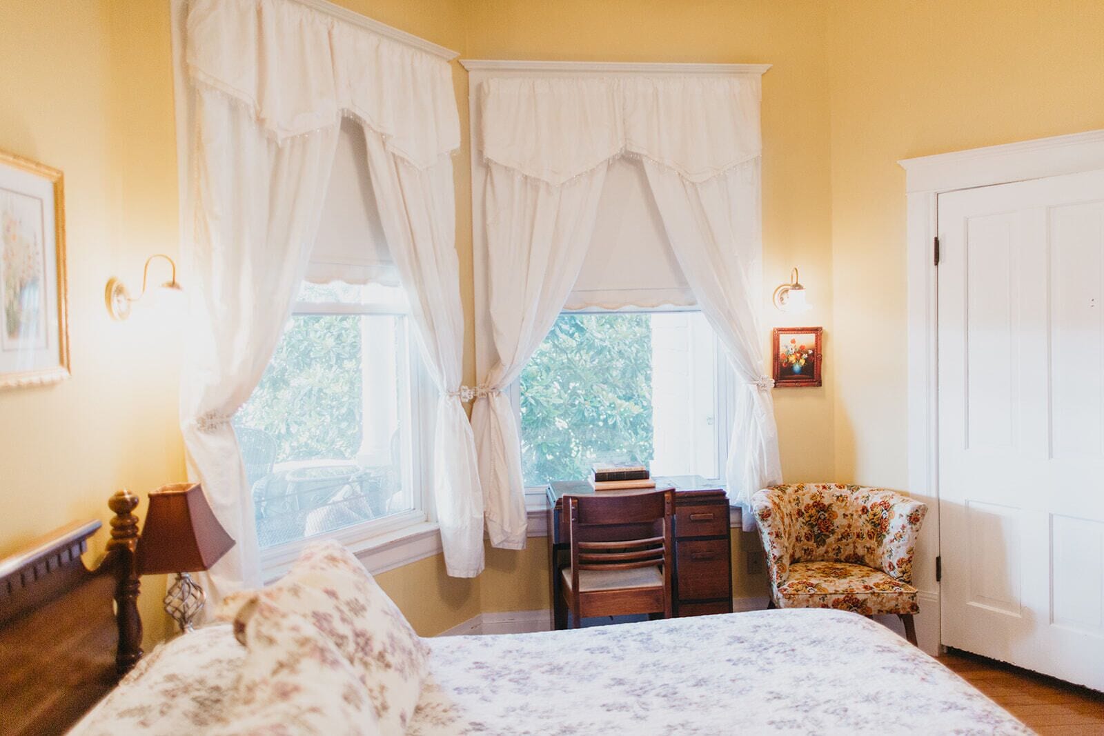 A bedroom with a bed, a chair, a desk, and a window with curtains.