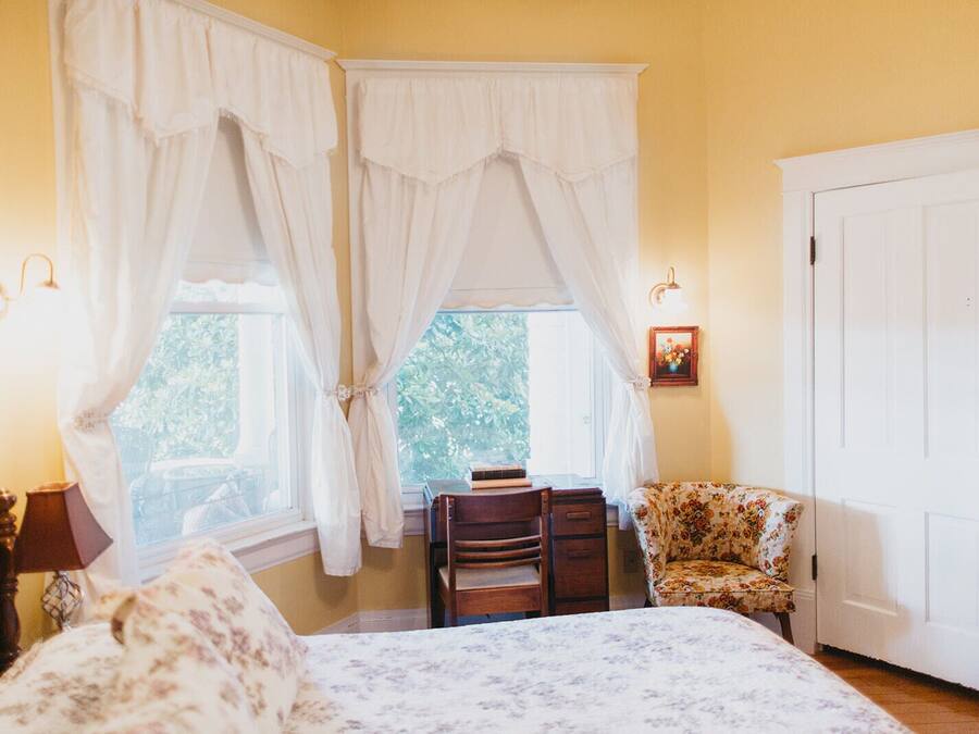 Een slaapkamer met een bed, een stoel, een bureau en een raam met gordijnen.