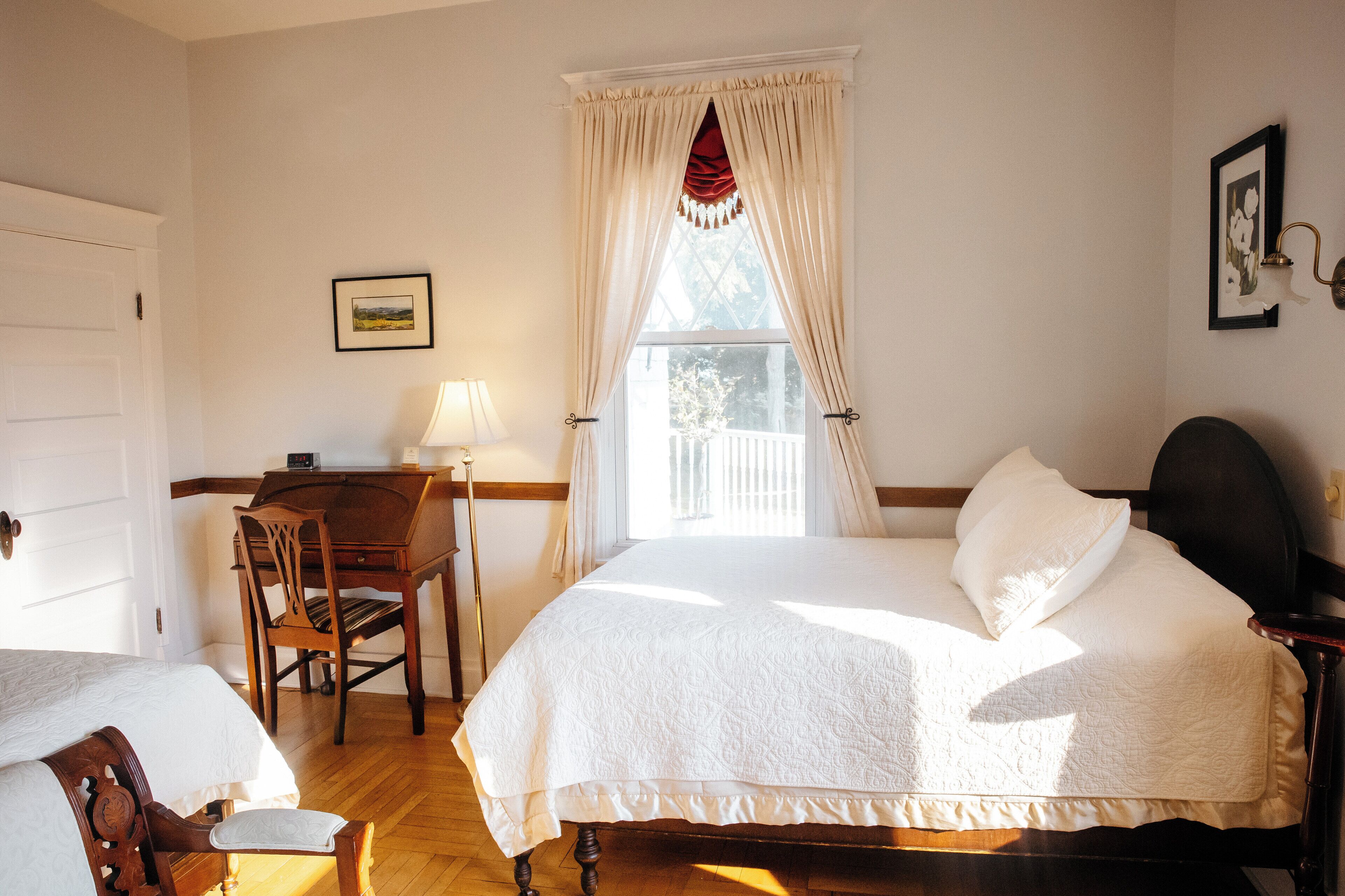 A bedroom with a bed, a desk, a chair, and a window with curtains.