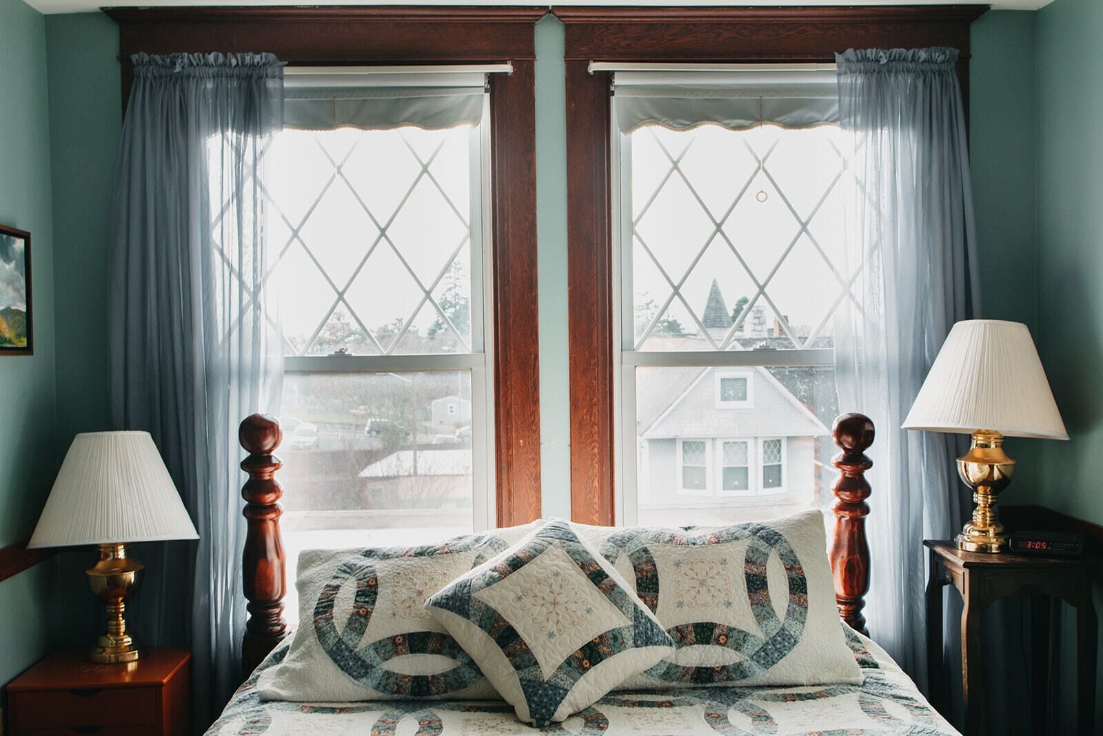A bedroom with a bed, two bedside tables, two lamps, and a window with curtains.