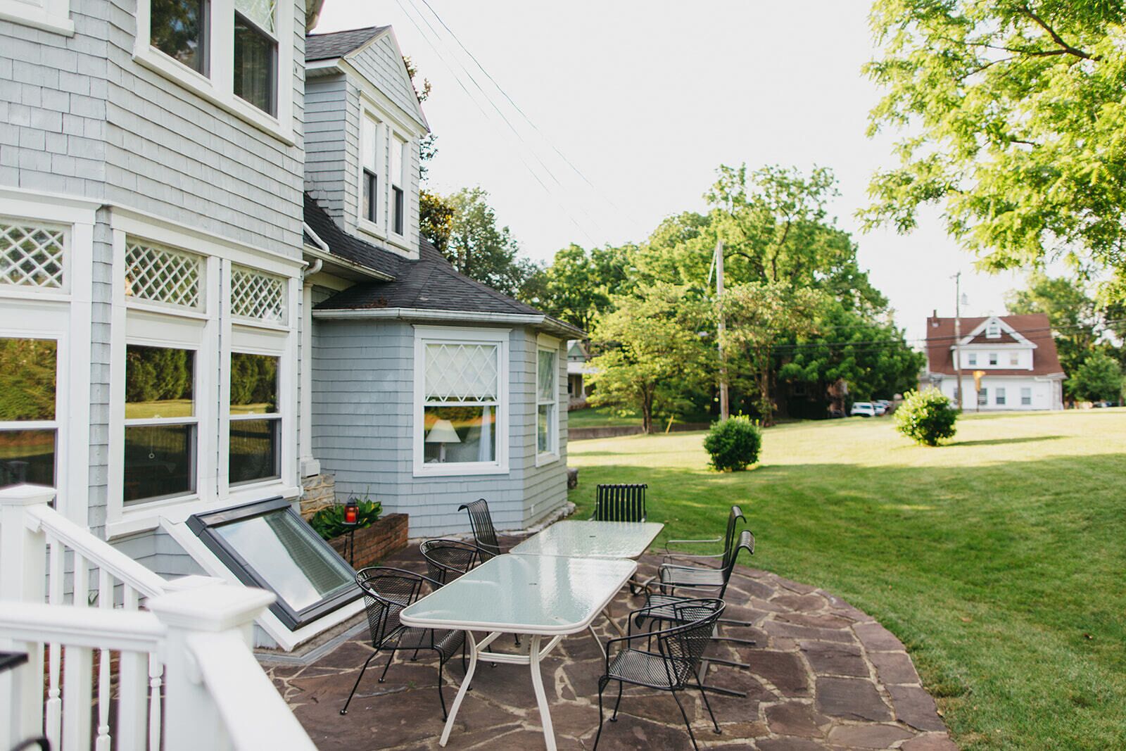 A house with a patio featuring a glass-top table and chairs, surrounded by a stone patio and a well-maintained lawn.
