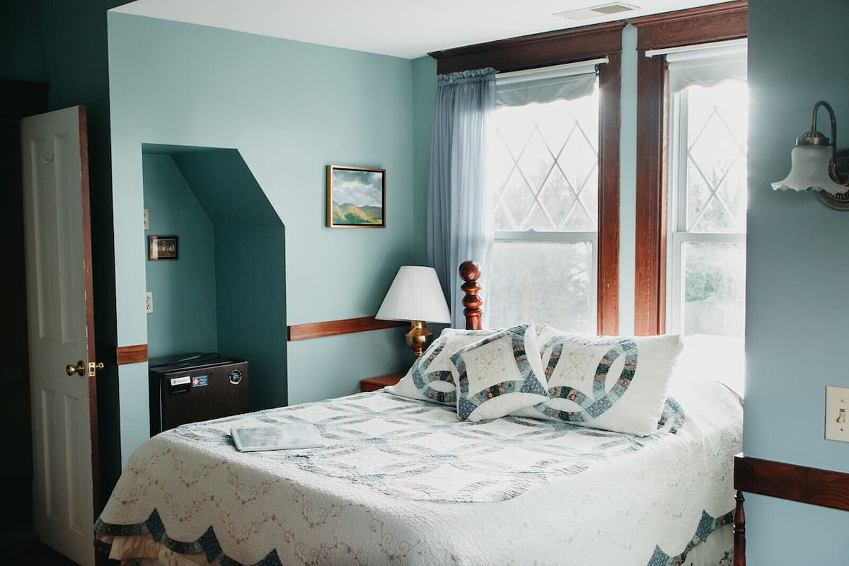 A bedroom with a bed, a nightstand, a lamp, a window with curtains, and a door.