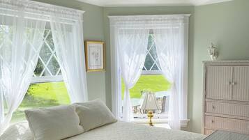 A bedroom with a bed, a glass-top dresser, a ceiling fan, and two windows with white curtains.