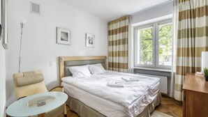 Ein Hotelzimmer mit Bett, Stuhl, kleinem Tisch und einem Fenster mit Vorhängen.