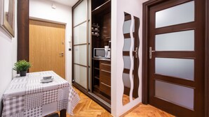 Ein Zimmer mit Holztür, einer auf einem Regal stehenden Mikrowelle, einem Tisch mit kariertem Tischläufer und einem Blumentopf.