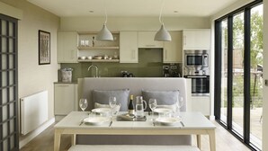 A modern kitchen with a dining area, featuring a large table set for four, a bench, and a view of the outdoors. - Treehouse Hotel - At Port Lympne Reserve (Hythe)