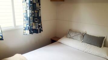 Een slaapkamer met een enkel bed, een nachtkastje en een raam met gordijnen.