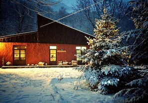 A snow-covered building with a red exterior, large windows, and a snow-covered tree in front. - Camping Aigües Braves (Llavorsi)