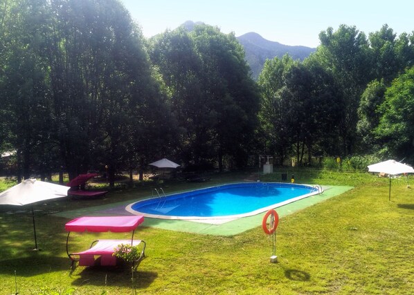 A swimming pool surrounded by grass and trees, with a mountain in the background. - Camping Aigües Braves (Llavorsi)