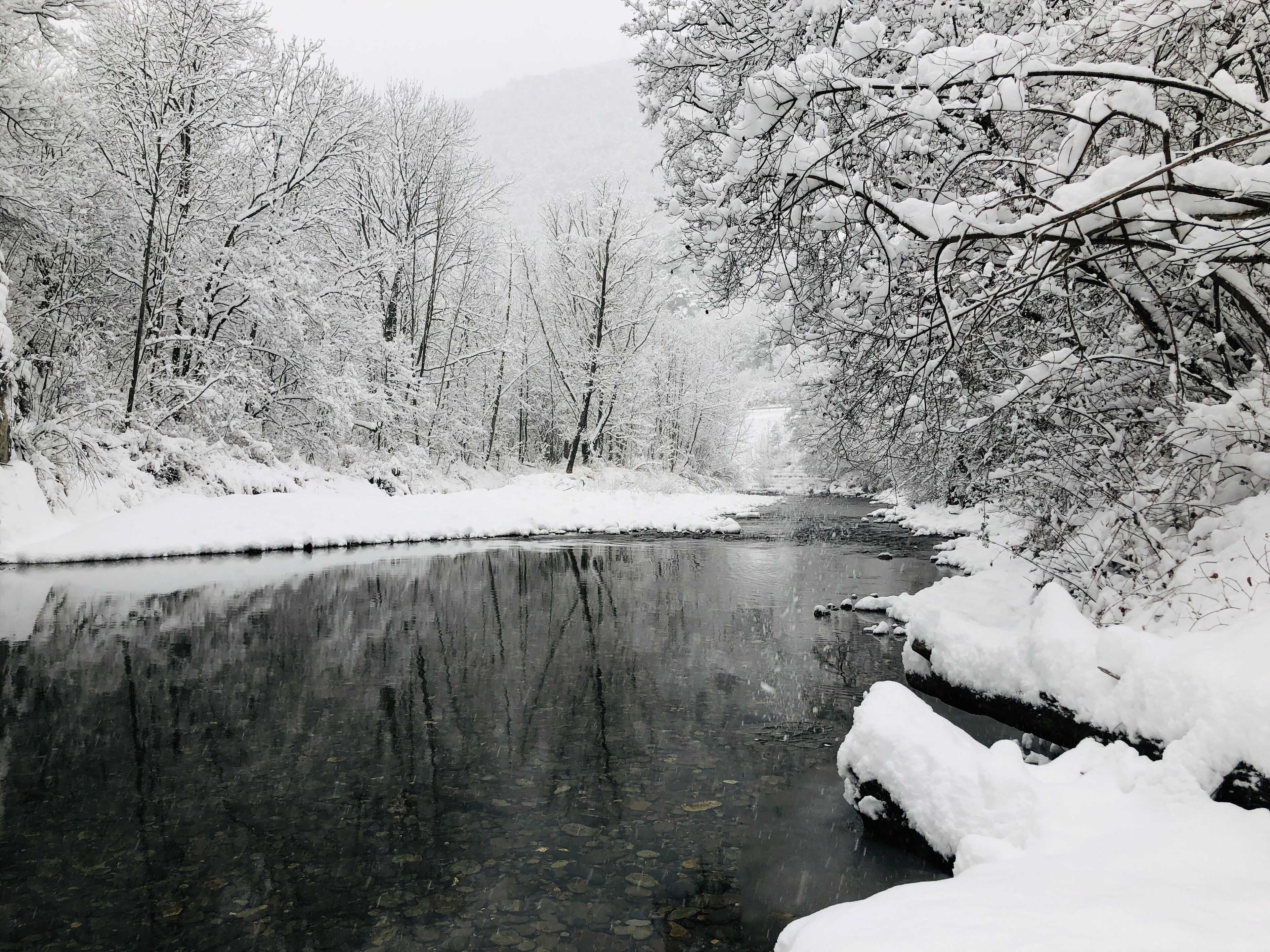 A snow-covered landscape with a river reflecting the trees and sky.