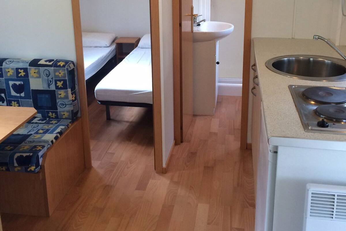 A compact kitchenette with a sink, stove, and a small bed.