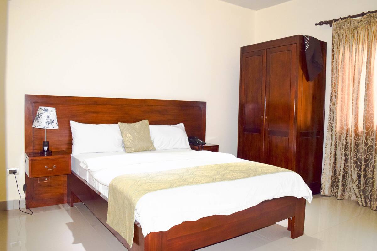 A bedroom with a wooden bed, bedside table, lamp, and wardrobe.