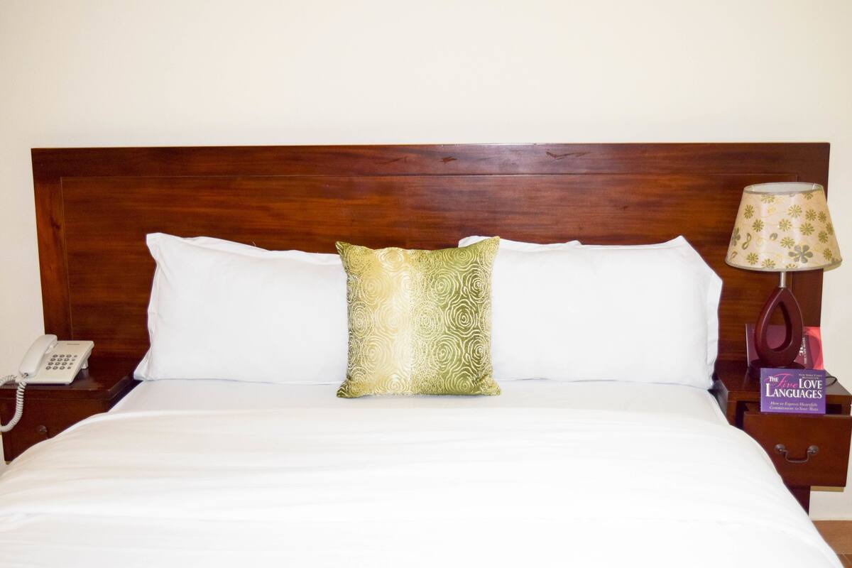 A neatly made bed with white linens, a wooden headboard, a patterned pillow, a bedside lamp, and a phone on a nightstand.