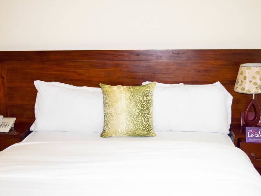 A neatly made bed with white linens, a wooden headboard, a patterned pillow, a bedside lamp, and a phone on a nightstand.
