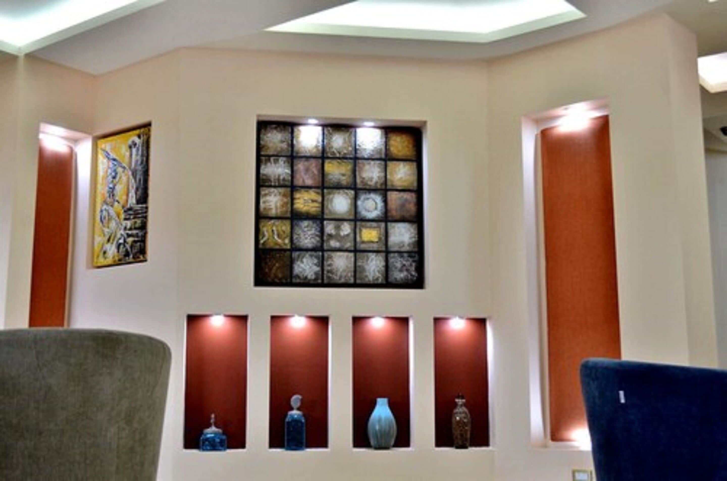 Una habitación con una lámpara de techo, una obra de arte en la pared, un ventanal de vitral y una estantería con objetos decorativos.