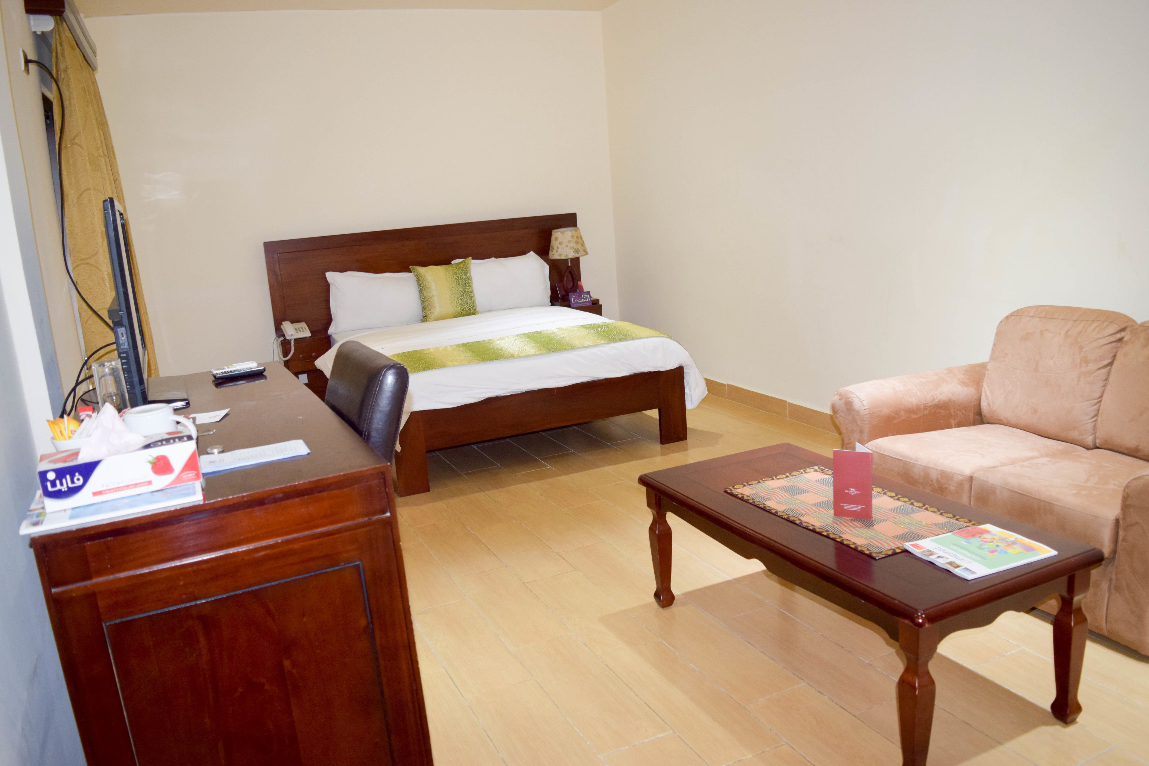 Ein Hotelzimmer mit einem hölzernen Bett, einem Schreibtisch aus Holz, einem beigefarbenen Sofa und einem gefliesten Boden.