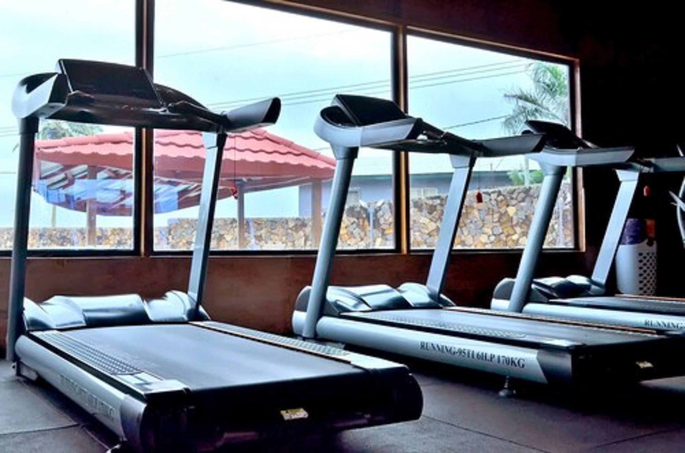 Drei Laufbänder in einem Fitnessstudio mit großen Fenstern und Blick auf Außenanlagen.
