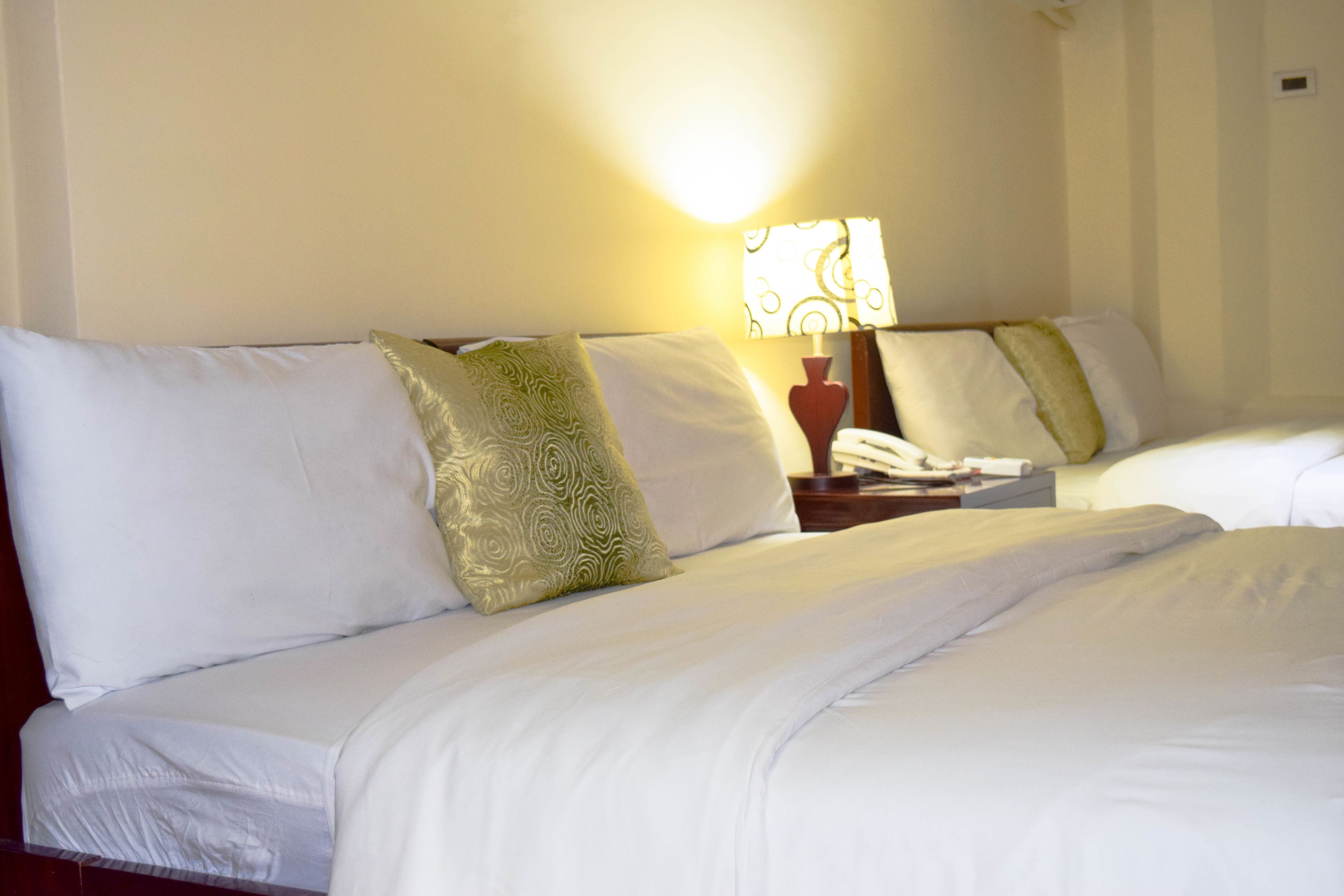 A hotel room with two beds, white linens, and a lamp on the nightstand.