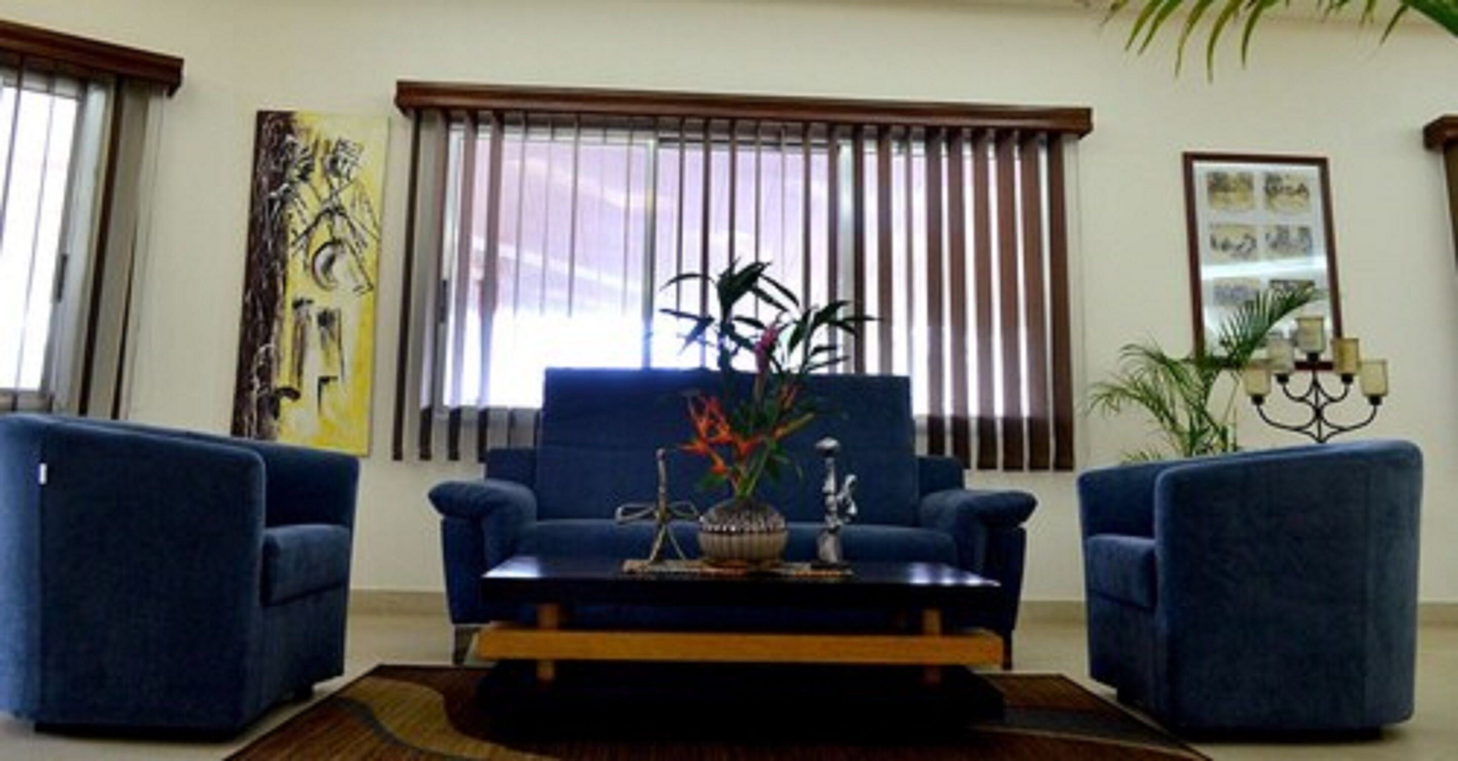 A living room with a blue sofa set, a coffee table, and a large window with blinds.