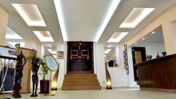 A hotel lobby with a reception desk, a staircase leading to the upper floor, and a large window at the top. - The Cape Hotel (Monrovia)