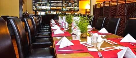 A restaurant with a long table set for a meal, surrounded by leather chairs.