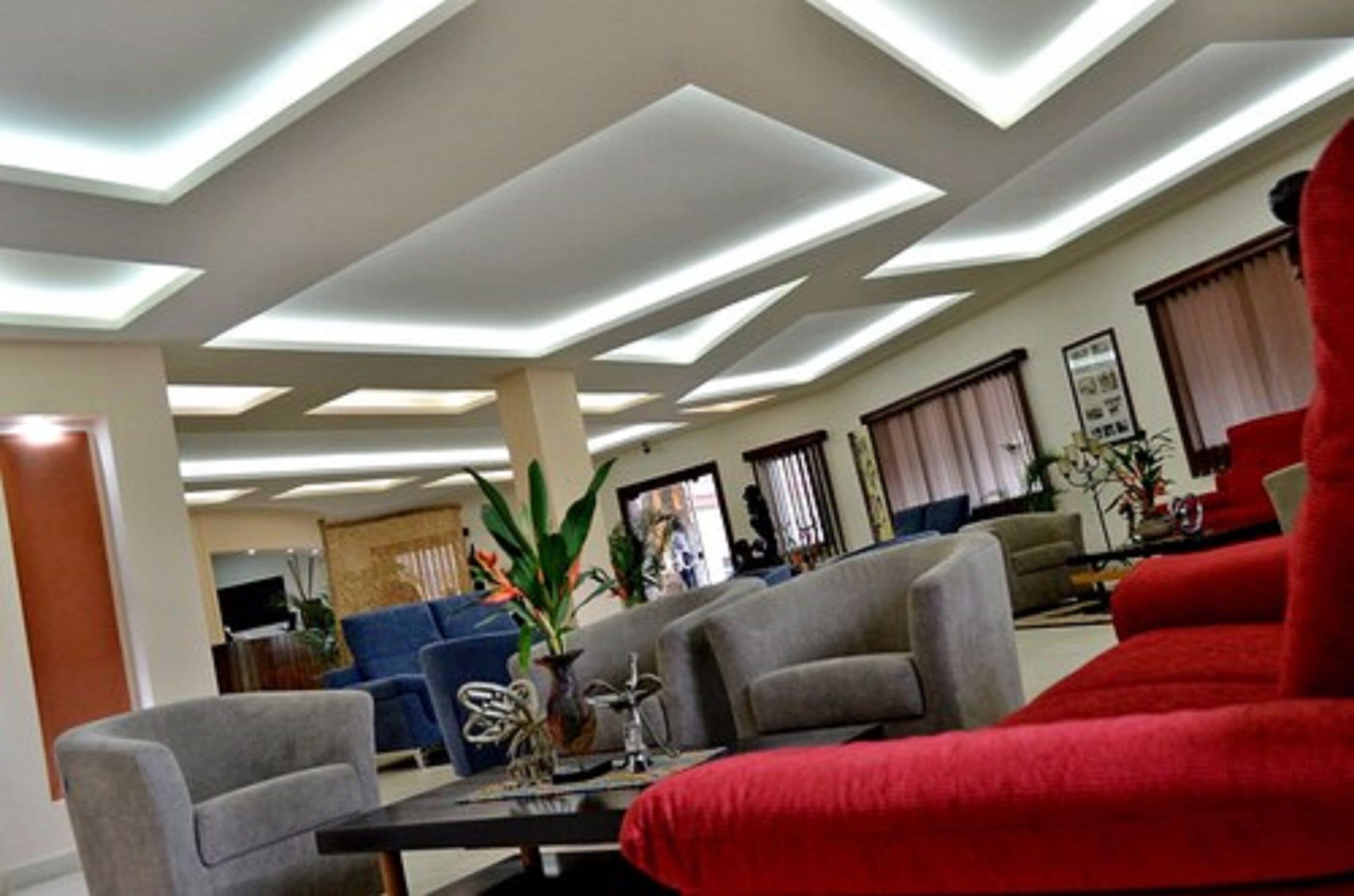 A modern living room with a sectional sofa, a coffee table, and a TV. The room has a high ceiling with recessed lighting.