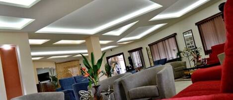 A modern living room with a sectional sofa, a coffee table, and a TV. The room has a high ceiling with recessed lighting.