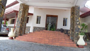 A building entrance with stone pillars, a glass door, and a staircase leading to a second floor. - The Cape Hotel (Monrovia)