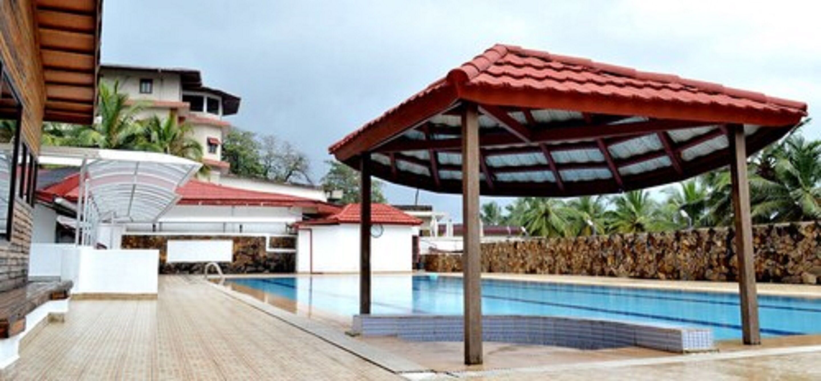 A swimming pool area with a covered pavilion, a brick pathway, and a stone wall.